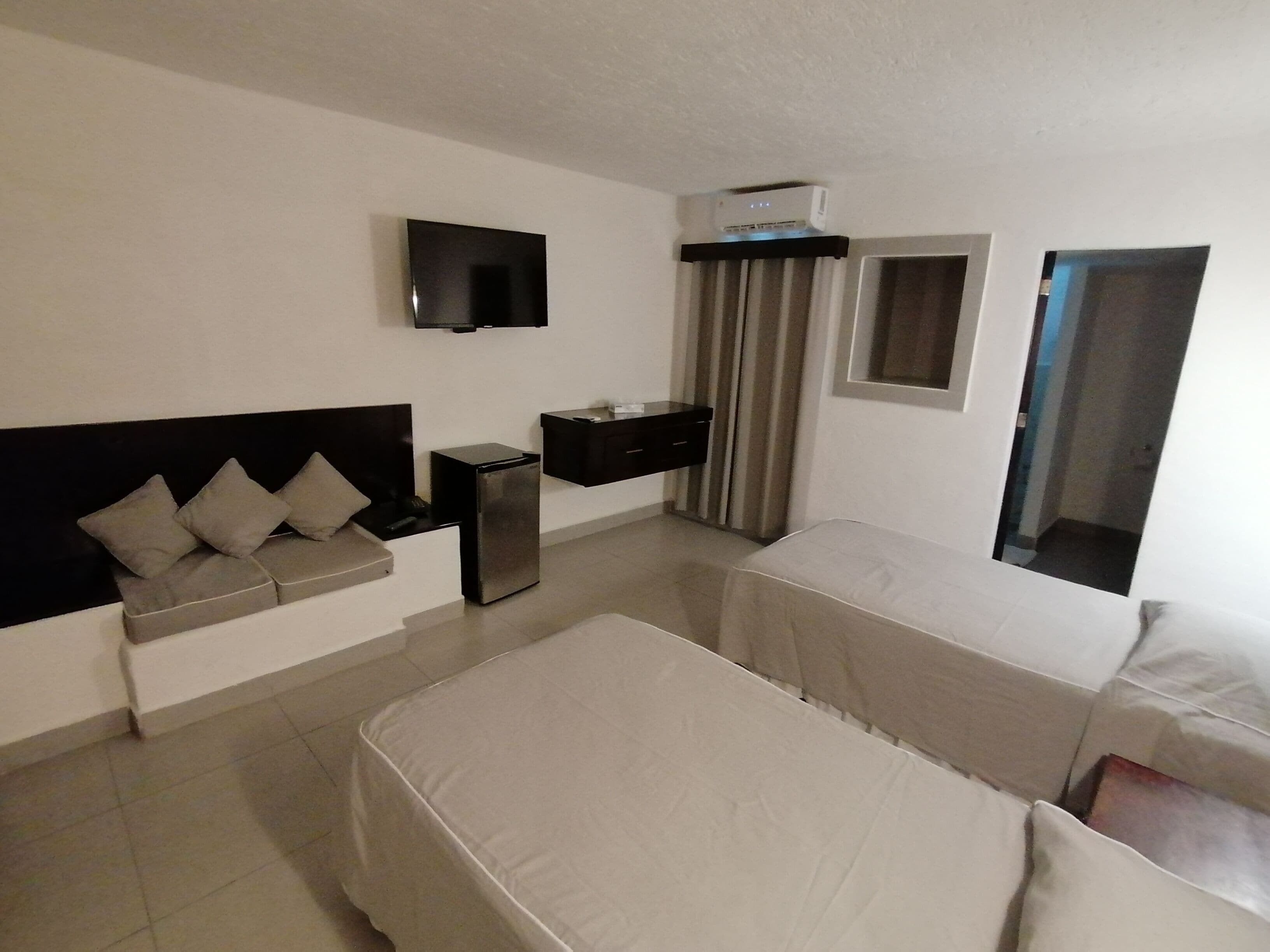 A hotel room with two beds, a TV, a small desk, and a window with curtains.