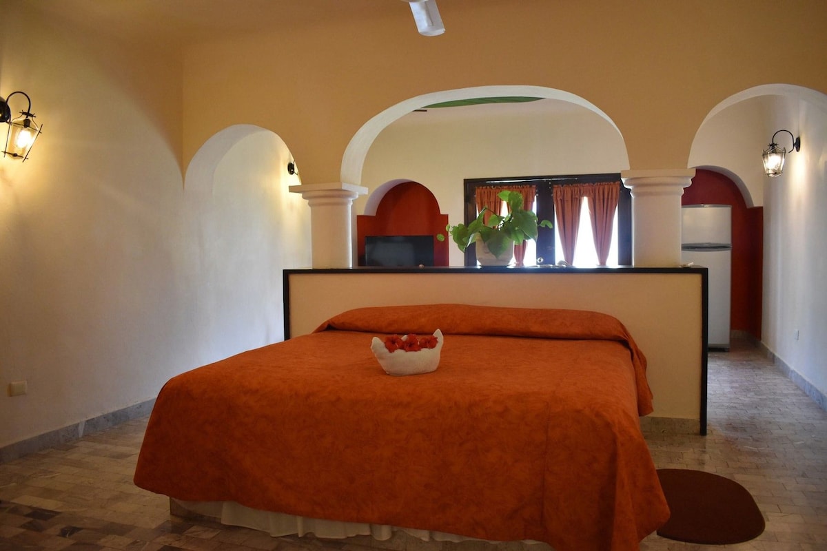 Ein Hotelzimmer mit Bett, Schreibtisch und Blick auf die Küche durch einen Bogen.