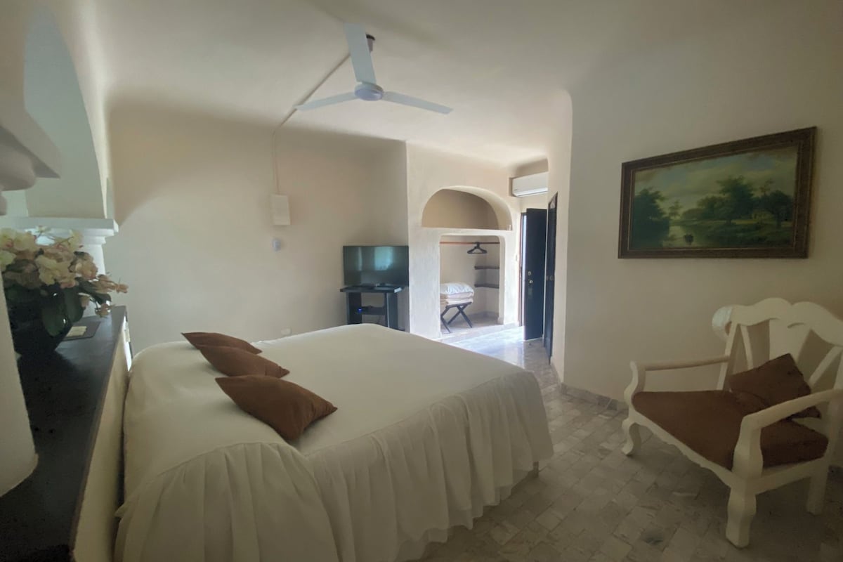 Ein Hotelzimmer mit einem Bett, einem Sessel, einem Schreibtisch mit Computer, einem Fernseher und einem Bild an der Wand.