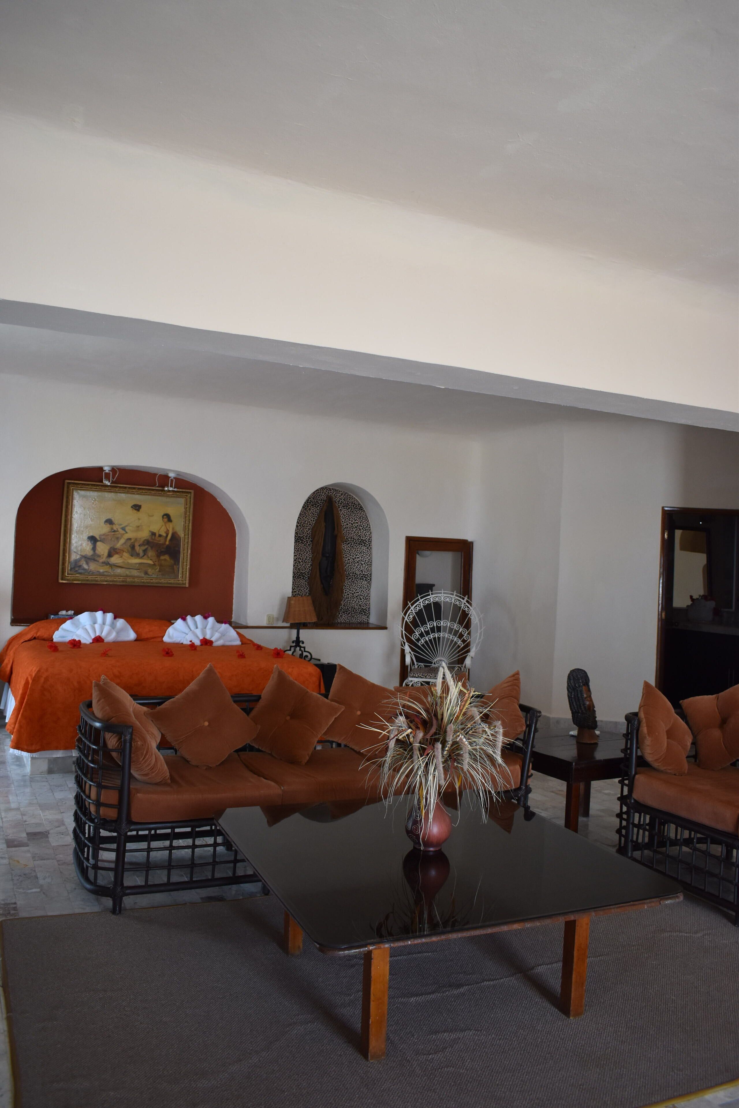 A hotel room with a bed, a sofa, a coffee table, and a mirror.
