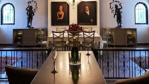 A dining area with a large chandelier, two ceiling fans, and a table set for four with wine glasses and a vase of flowers. - Villablanca Garden Beach Hotel (Cozumel)