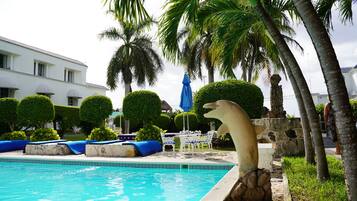 A swimming pool with lounge chairs and umbrellas, surrounded by palm trees and a building.