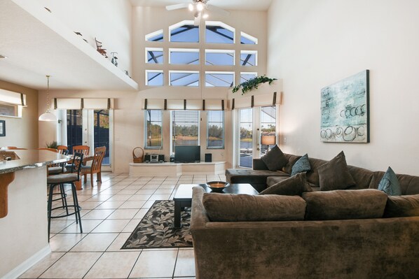 A spacious living area with a large couch, a dining table, and a kitchen area with a bar. - Advantage Vacation Homes (Kissimmee)