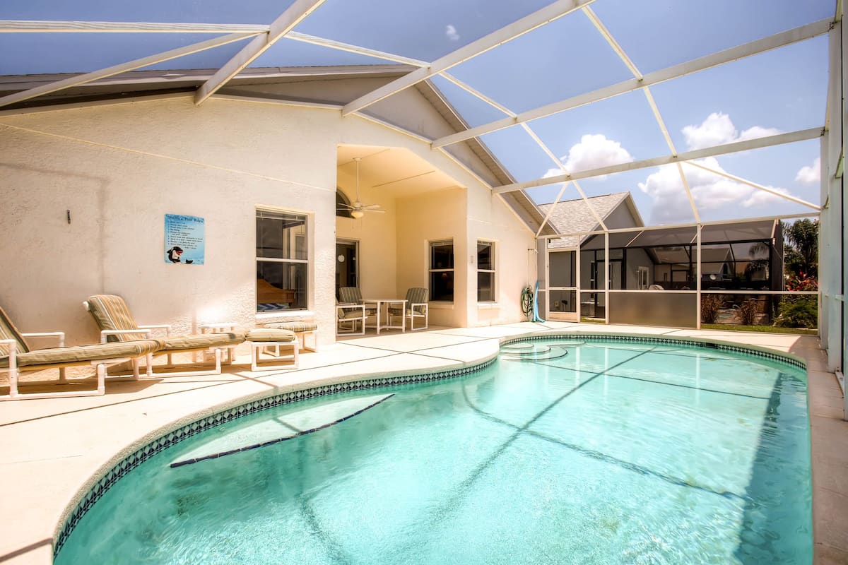 Ein Schwimmbecken mit überdachter Terrasse, Liegestühlen und einer Dachkonstruktion.
