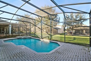 A swimming pool with a glass enclosure, surrounded by a brick patio and a grassy area. - Advantage Vacation Homes (Kissimmee)