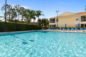 A clear swimming pool with blue water, surrounded by lounge chairs and umbrellas, with a building in the background. - Advantage Vacation Homes (Kissimmee)