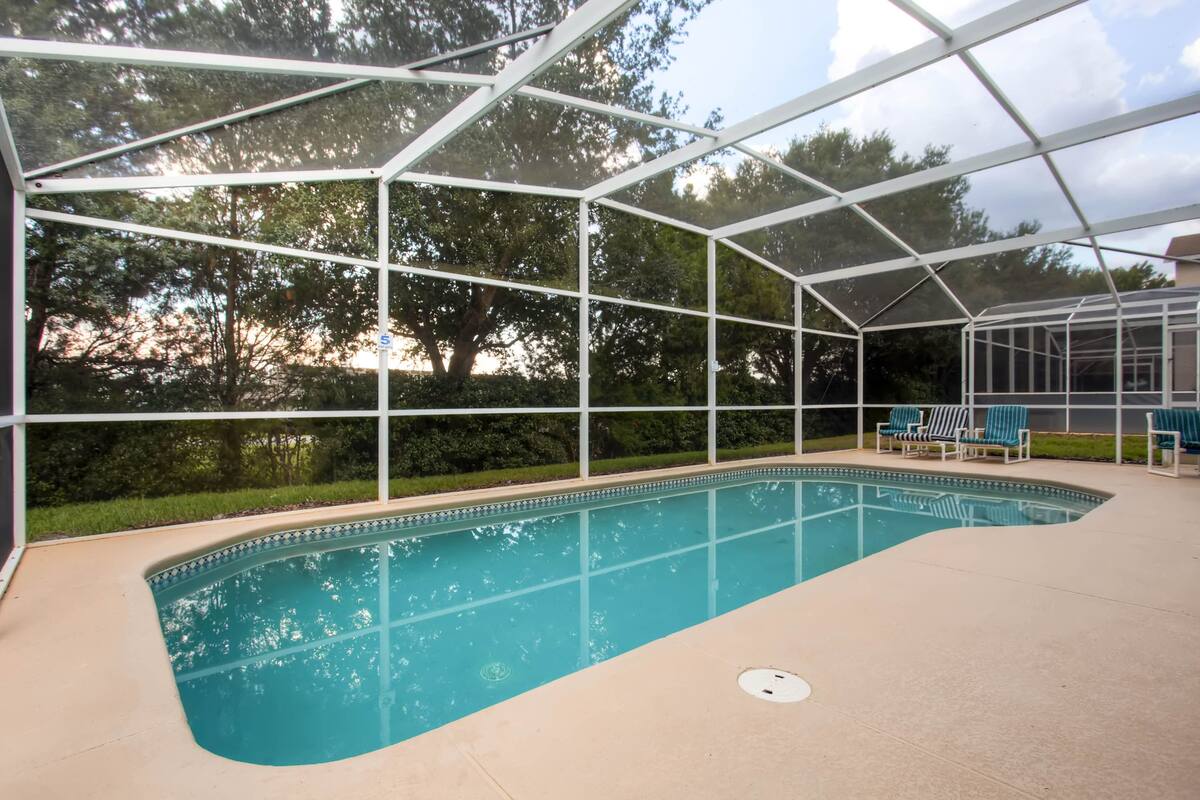 Ein überdachter Pool im Freien mit Glasveranda, umgeben von Rasenflächen und Bäumen.