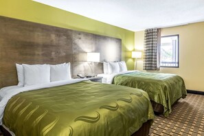 A hotel room with two beds, a wooden headboard, a window with curtains, and a nightstand with a lamp.