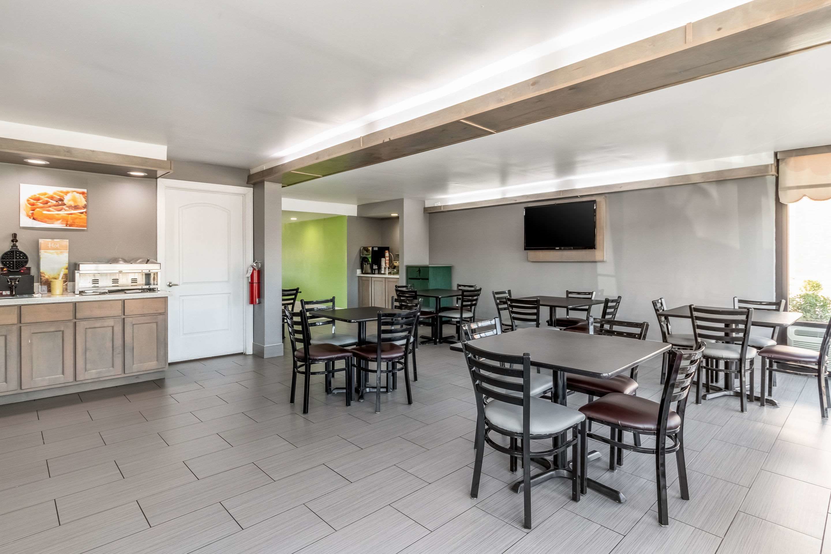 A modern dining area with multiple tables and chairs, a kitchen area with a coffee machine, and a fire extinguisher on the wall.