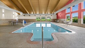 Une piscine intérieure avec de grandes baies vitrées offrant une vue dégagée sur l’extérieur, entourée d’espaces de détente et dotée d’un plafond couvert.