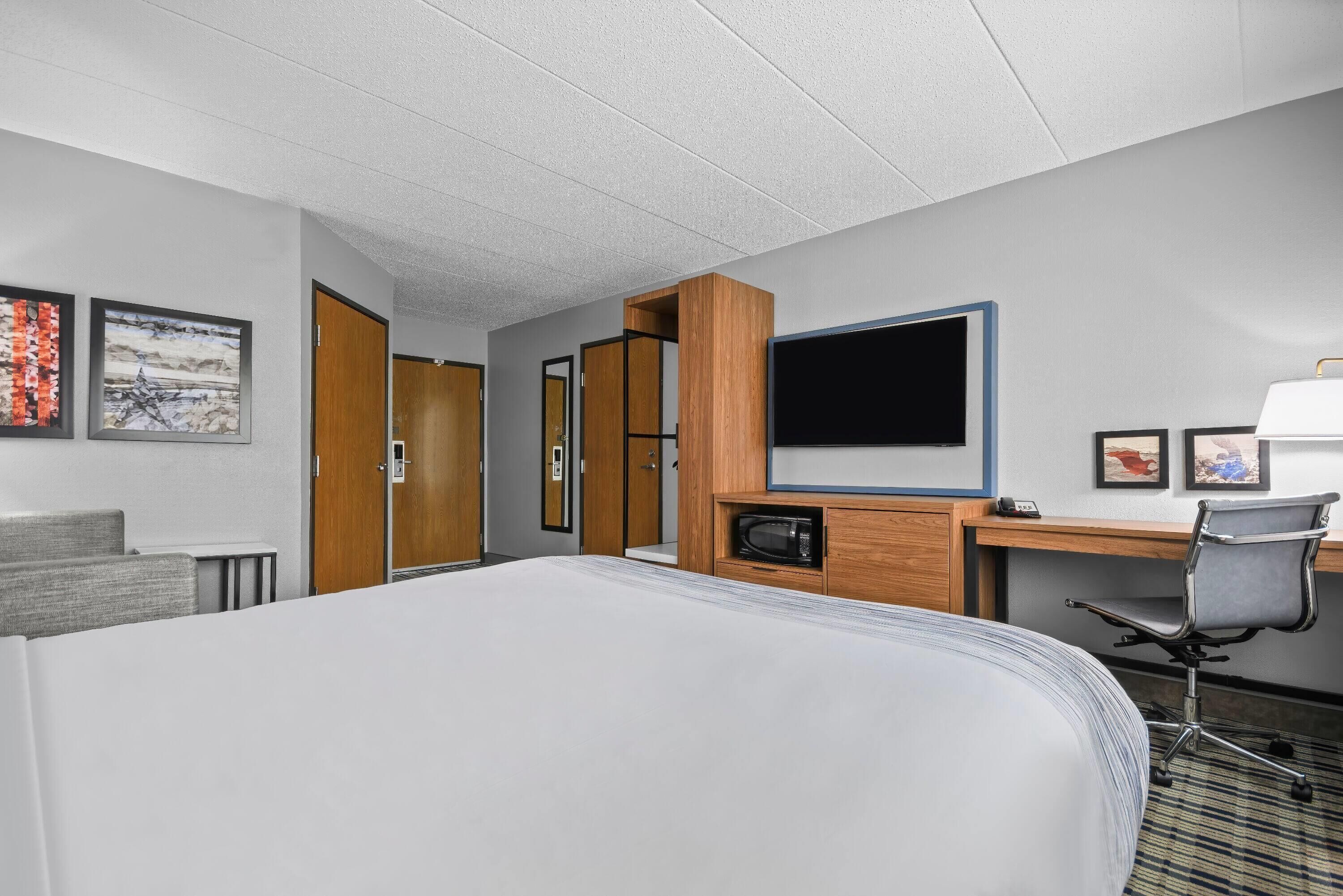 A hotel room with a bed, a desk with a computer, a TV, and a chair.