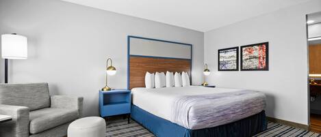 A hotel room with a bed, a chair, a nightstand, a lamp, and a wall with two framed pictures.