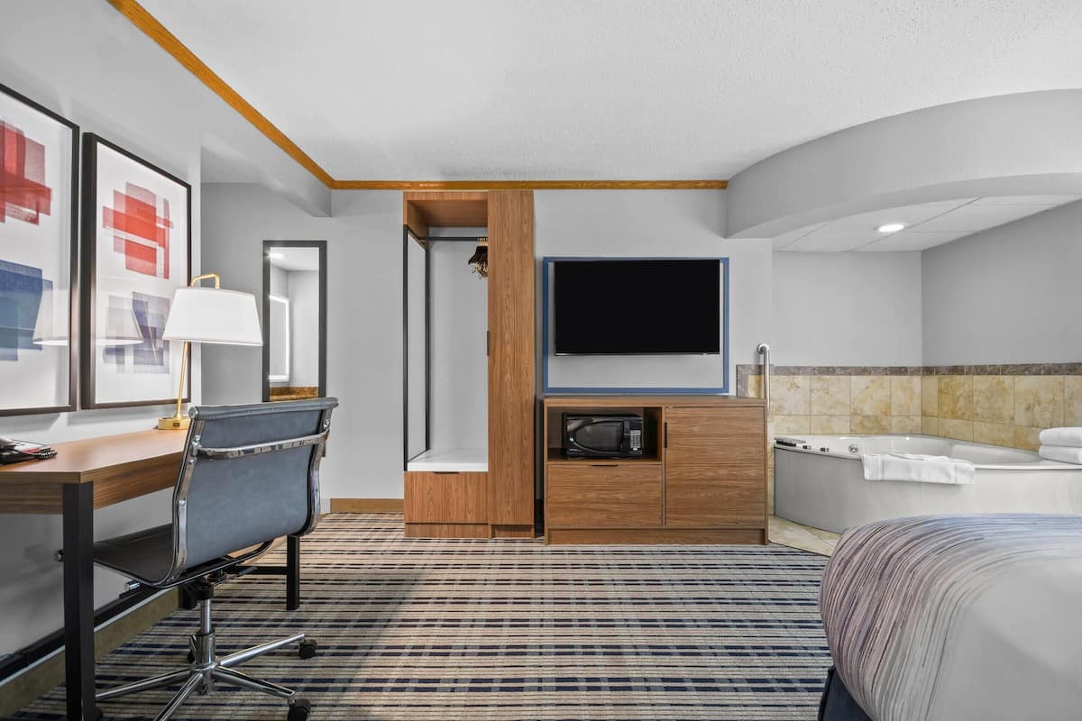 Habitación de hotel con cama, escritorio con silla, televisor, microondas, armario, ducha y bañera.