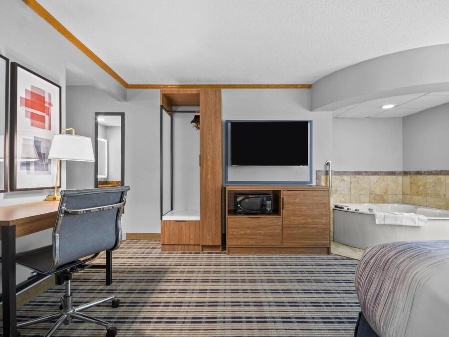 Une chambre d’hôtel comprenant un lit, un bureau avec une chaise, une télévision, un four à micro-ondes, un placard, une douche et une baignoire.