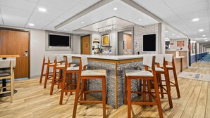 Un espace bar moderne doté d’un îlot central, de tabourets de bar, d’un téléviseur à écran plat et d’un mur recouvert de carreaux.