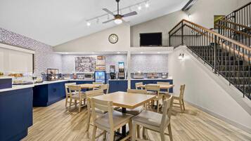 A modern restaurant with a high ceiling, a central island with kitchen appliances, and a staircase leading to an upper level.