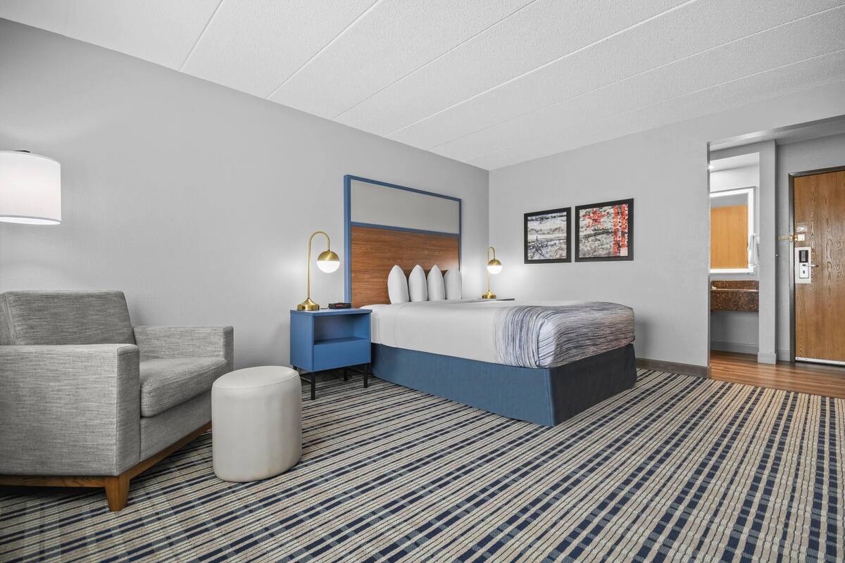 Una habitación de hotel moderna con una cama, una silla, una mesita de noche y un espejo grande.