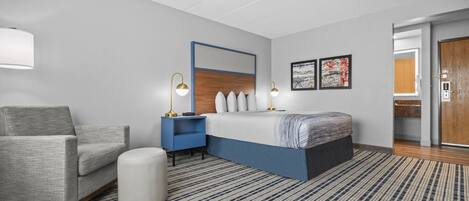A modern hotel room with a bed, a chair, a nightstand, and a large mirror.