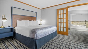 Une chambre d’hôtel avec un grand lit, des lampes de chevet, une tête de lit en bois, une salle de bain avec baignoire et une moquette à motifs.