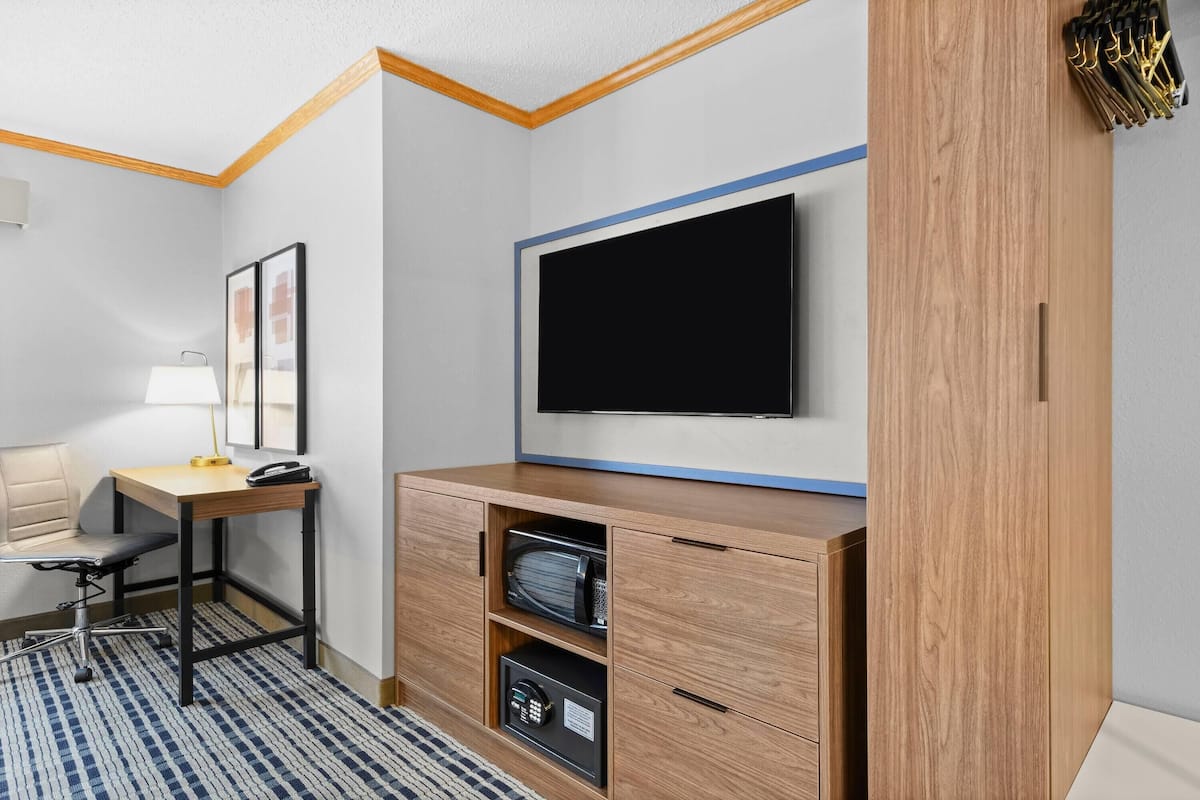 Habitación de hotel con escritorio de madera, una silla, televisor de pantalla plana en la pared, una caja fuerte y un mueble pequeño.