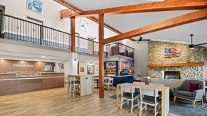 Un hall d’entrée spacieux avec un comptoir de réception, un plancher en bois, une cheminée en pierre et un balcon agrémenté de balustrades.