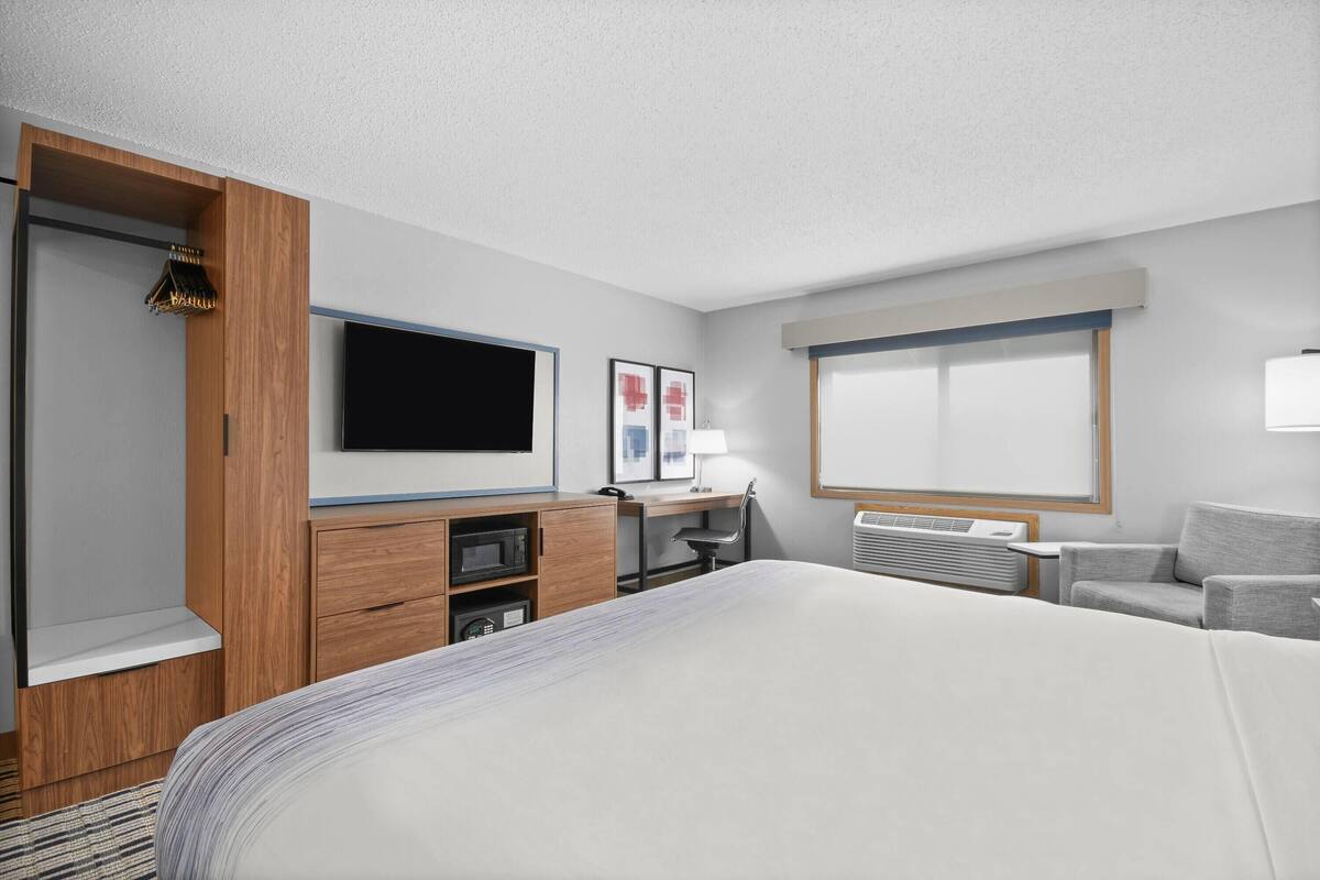 Una habitación de hotel con cama, escritorio, silla, televisor y ventana.