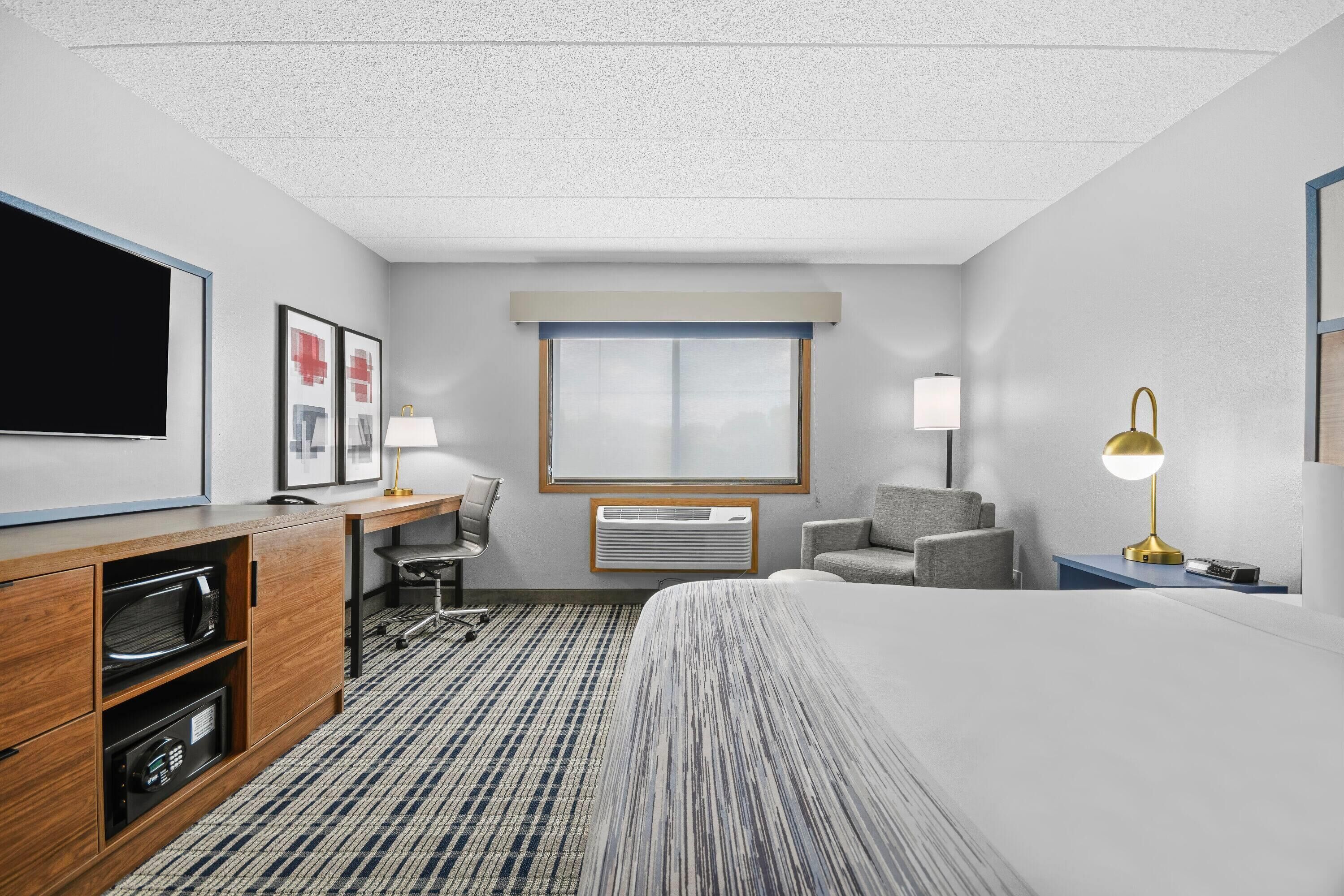 A hotel room with a bed, a desk with a computer, a chair, a TV, and a window.