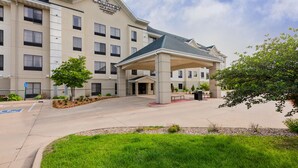A hotel with a covered entrance, multiple floors, and a landscaped area with grass and trees. - Staybridge Suites Cedar Rapids North by IHG (Cedar Rapids)