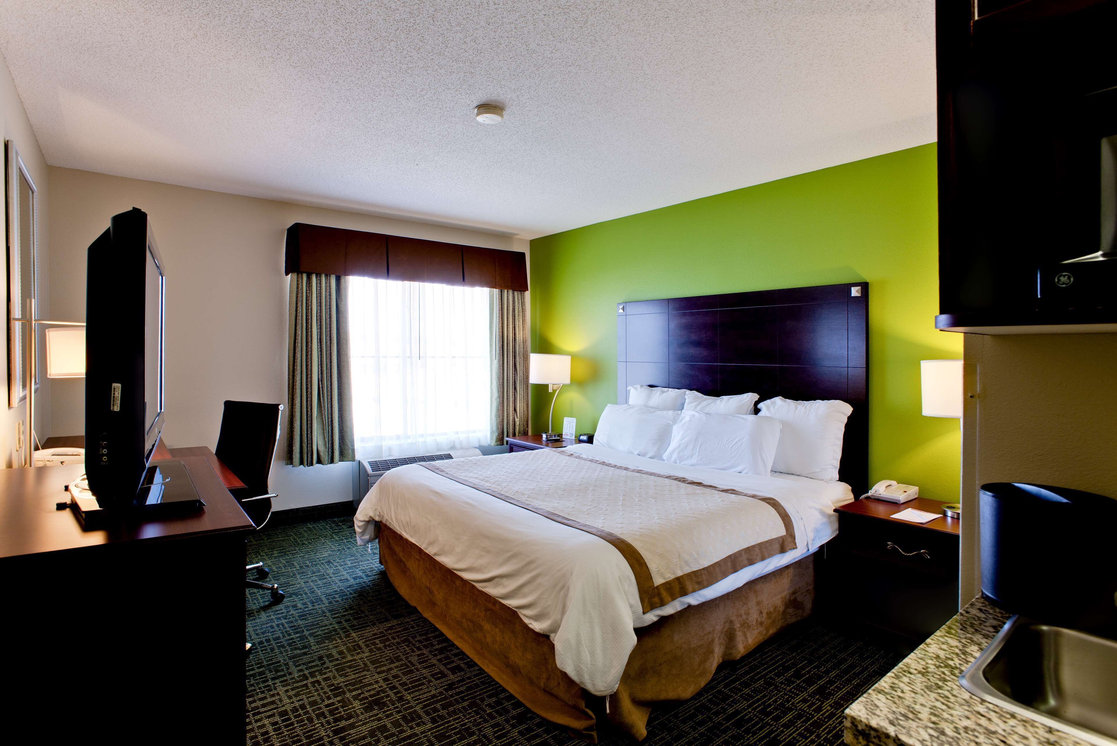 A hotel room with a large bed, a desk with a computer, a television, and a window with curtains.