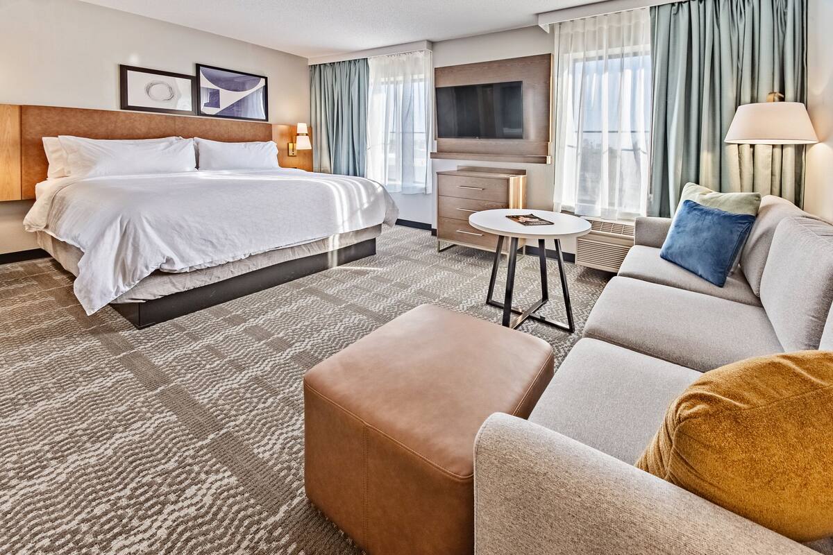 A hotel room with a bed, a sofa, a small table, and a TV.