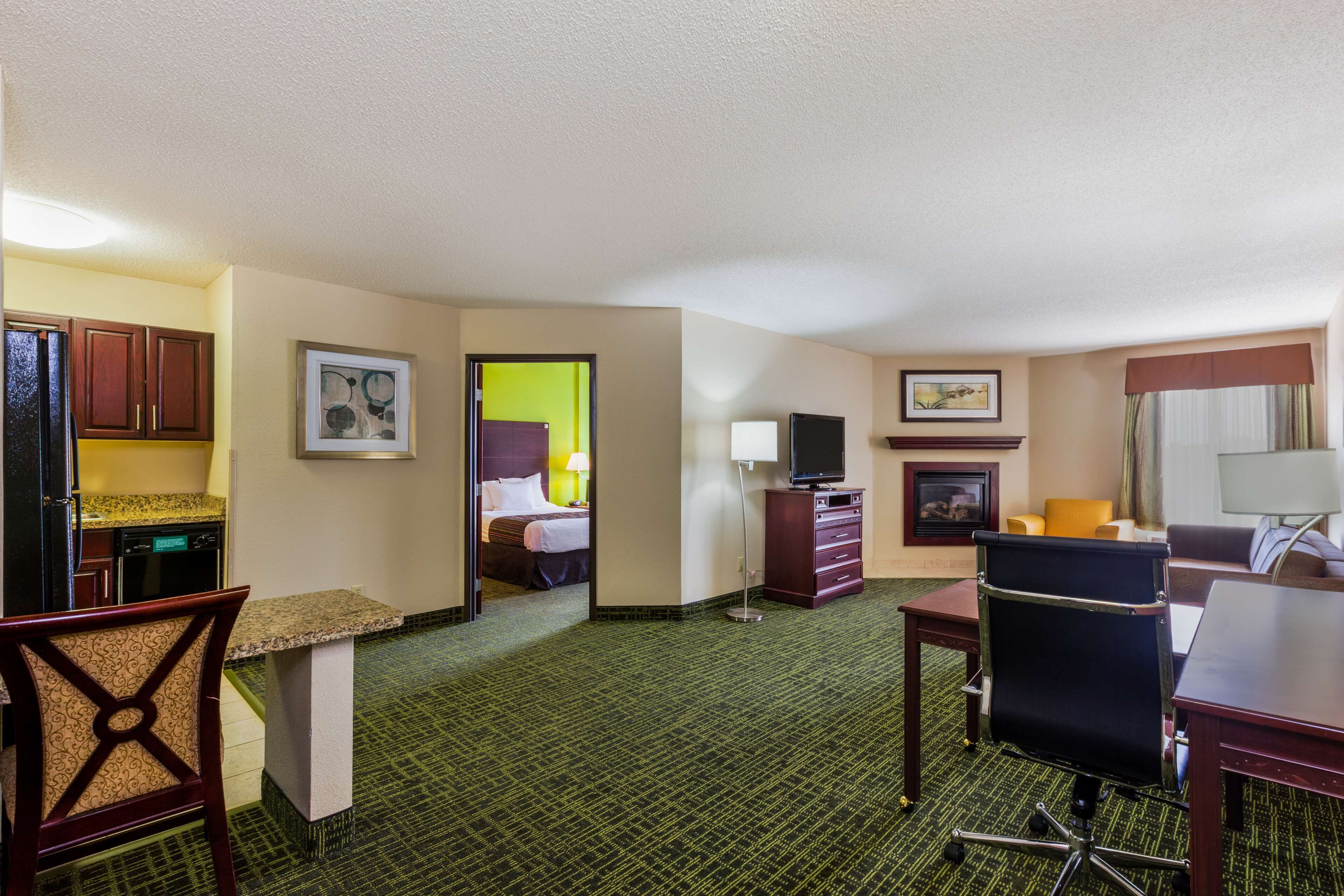Quarto de hotel com cozinha compacta, cama, escrivaninha, cadeira e televisão.