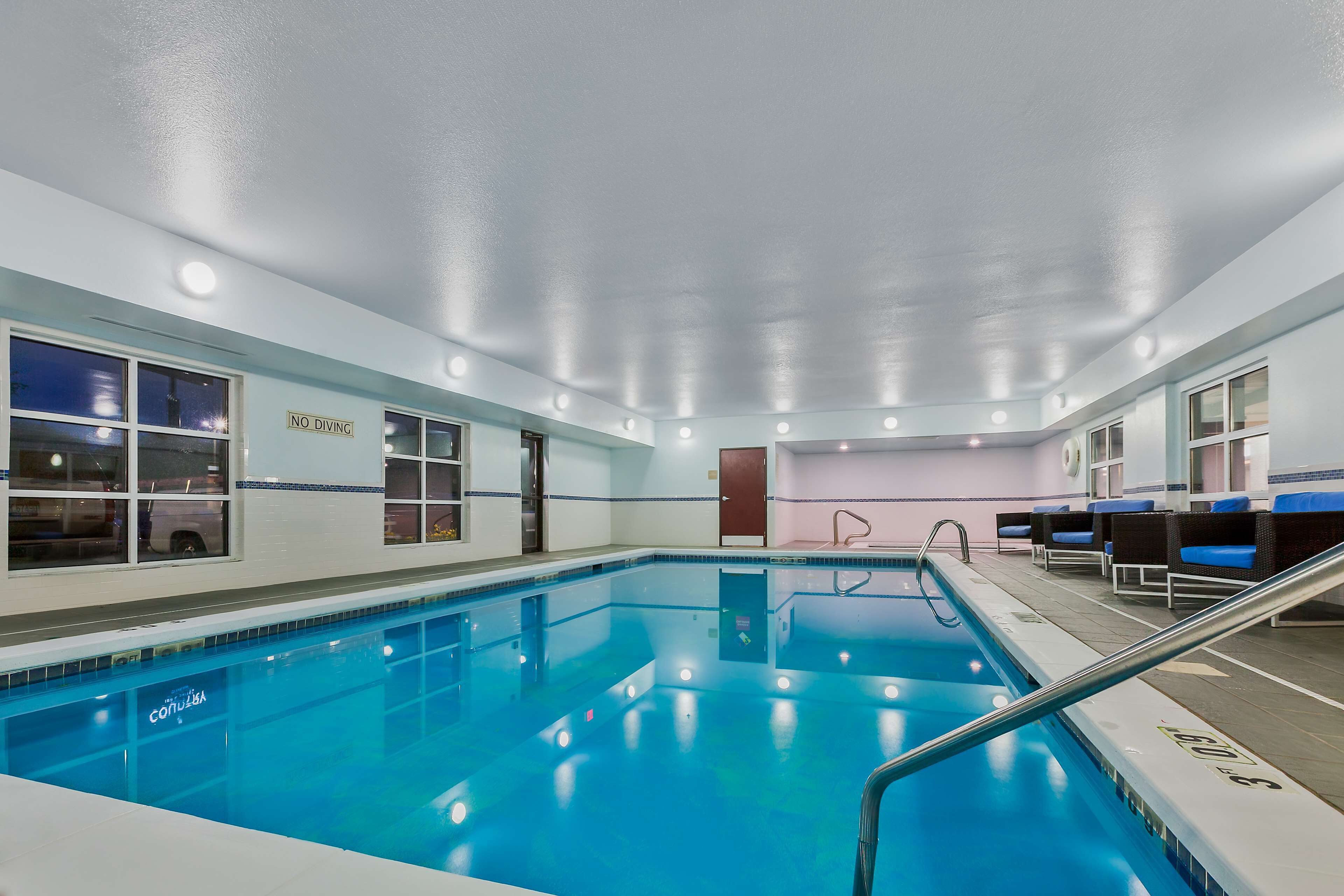 An indoor swimming pool with a 'No Diving' sign, seating area with blue cushions, and a 'Convida' logo on the pool edge.