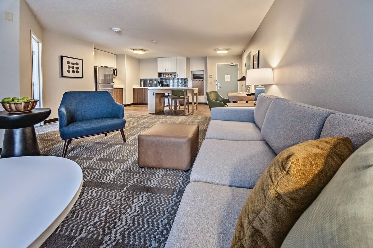 A modern living room with a sofa, ottoman, and a dining table with chairs.