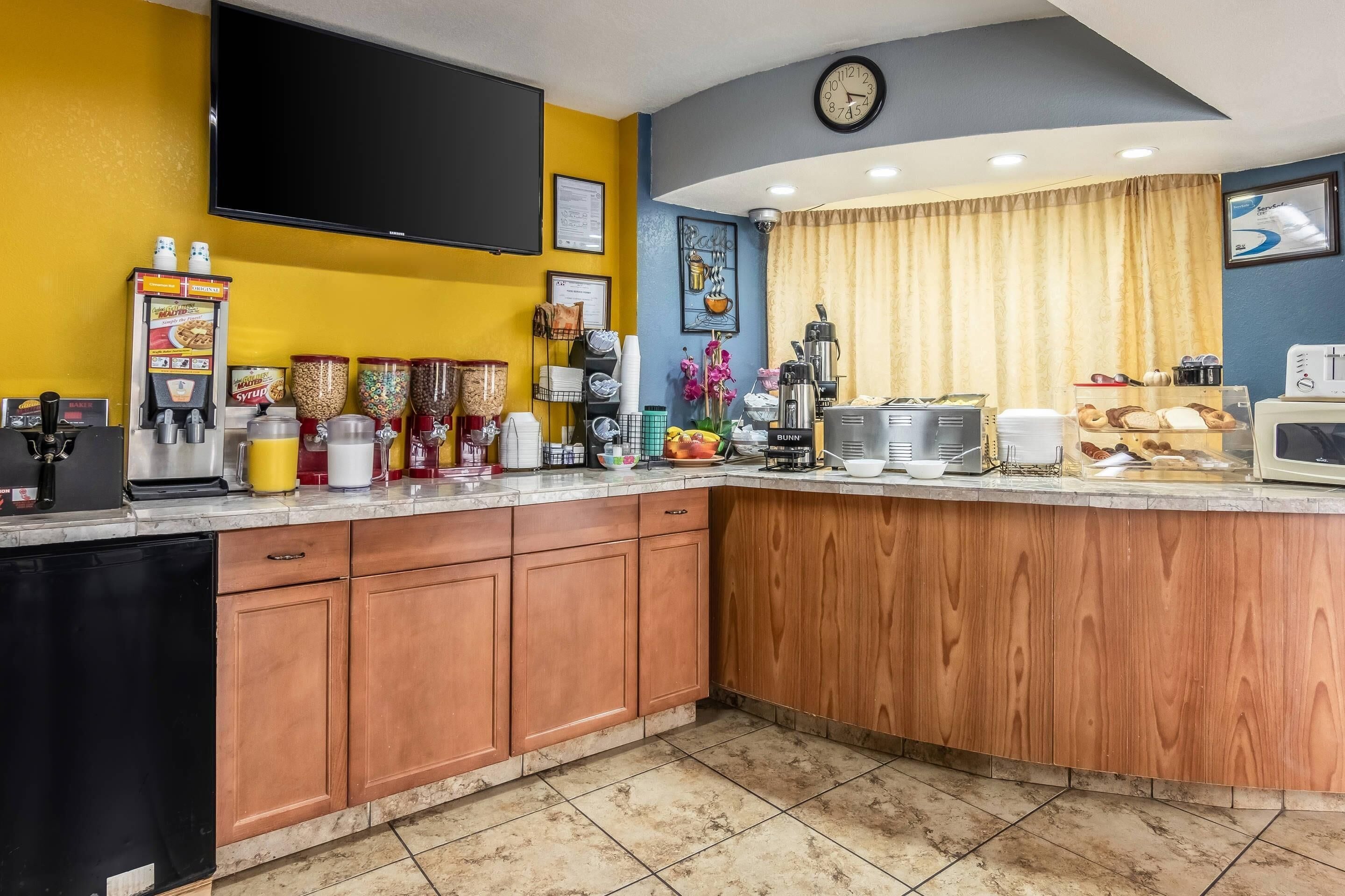 A kitchen with a bar area, equipped with coffee machines, a microwave, and a clock on the wall.