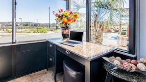 Una habitación moderna con un ventanal grande, una computadora portátil sobre el escritorio, un florero con flores y una bandeja decorativa con varios objetos.