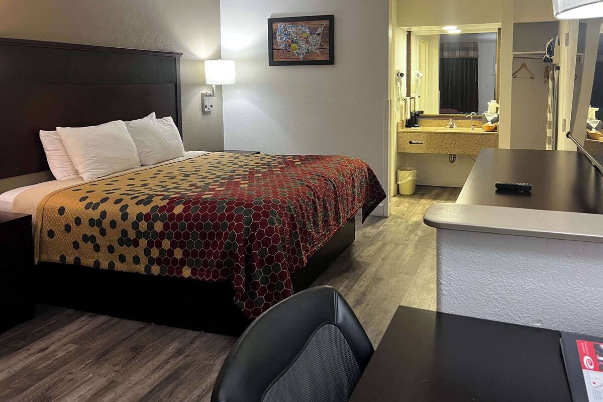 Ein Hotelzimmer mit einem Bett, einem Schreibtisch, einem Stuhl, einem Badezimmer mit Waschbecken und Spiegel sowie einer Karte an der Wand.
