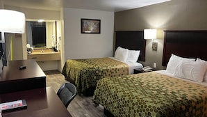 Habitación de hotel con dos camas, un escritorio, una silla, un espejo y una mesita de noche con lámpara.