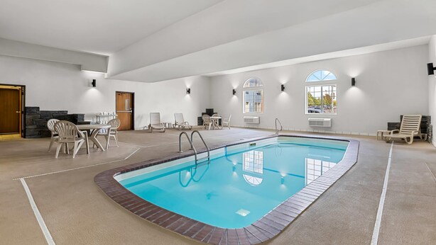 An indoor swimming pool with a clear blue water, surrounded by lounge chairs and a dining area. - Rodeway Inn Rapid City North (Rapid City)