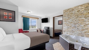 A hotel room with a large bed, a separate bathroom with a bathtub, a desk with a chair, and a TV mounted on the wall. - Rodeway Inn Rapid City North (Rapid City)