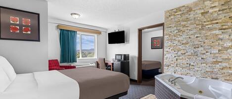 Habitación de hotel con una cama grande, baño independiente con bañera, escritorio con silla y televisión montada en la pared.