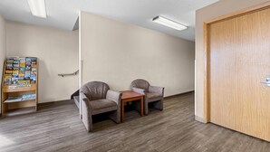 A room with two armchairs, a small wooden table, a bulletin board with travel information, and a wooden door. - Rodeway Inn Rapid City North (Rapid City)