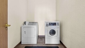 A laundry room with two washing machines and a dryer, a wooden door, and a dark rug on the floor. - Rodeway Inn Rapid City North (Rapid City)