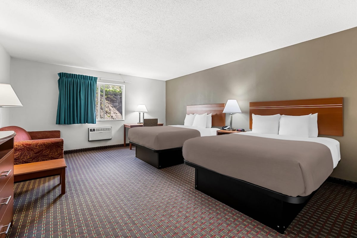 Une chambre d’hôtel avec deux lits, un bureau, une chaise et une fenêtre avec des rideaux.