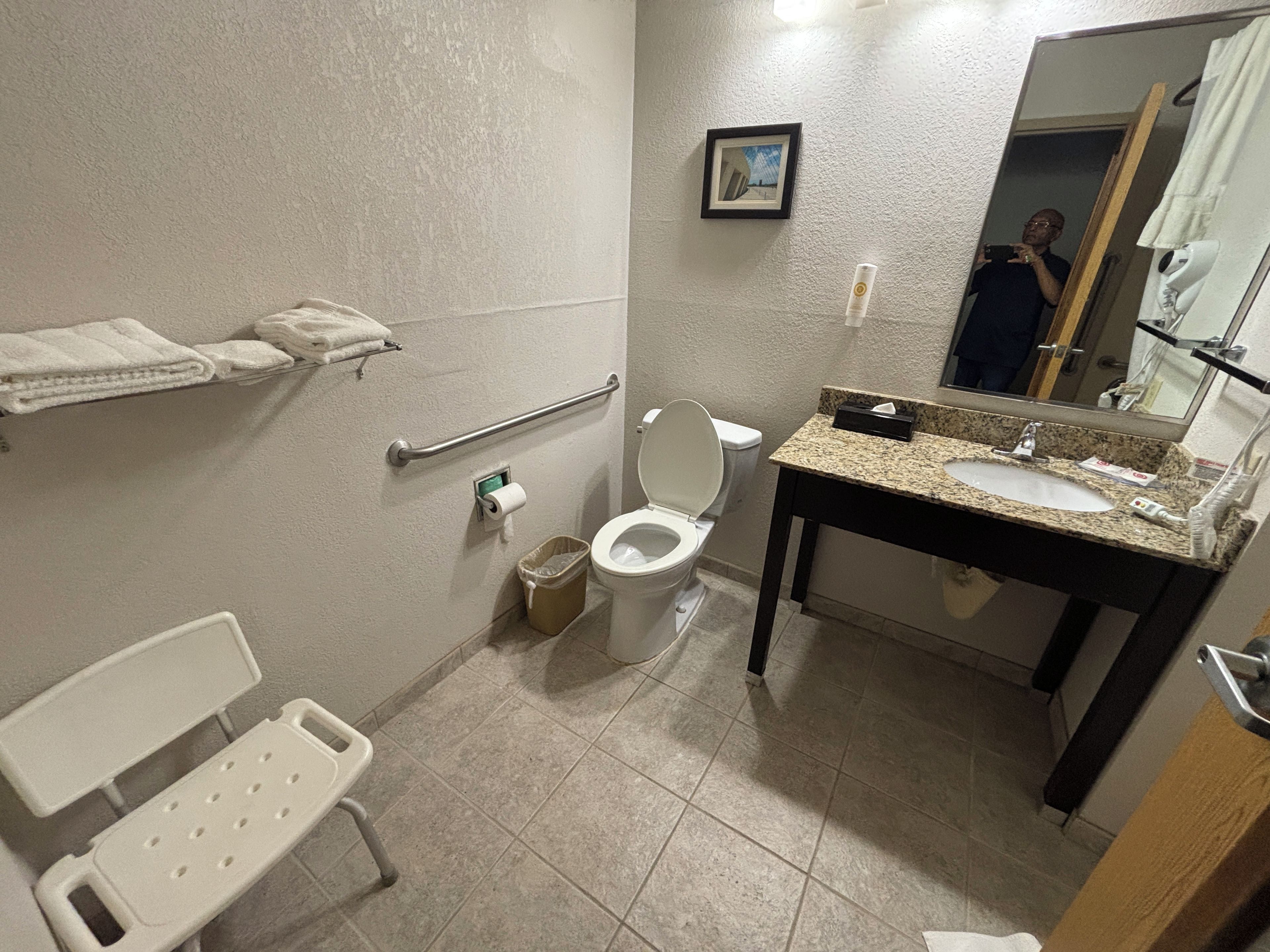 Een badkamer met toilet, wastafel, handgreep en een kleine prullenbak.