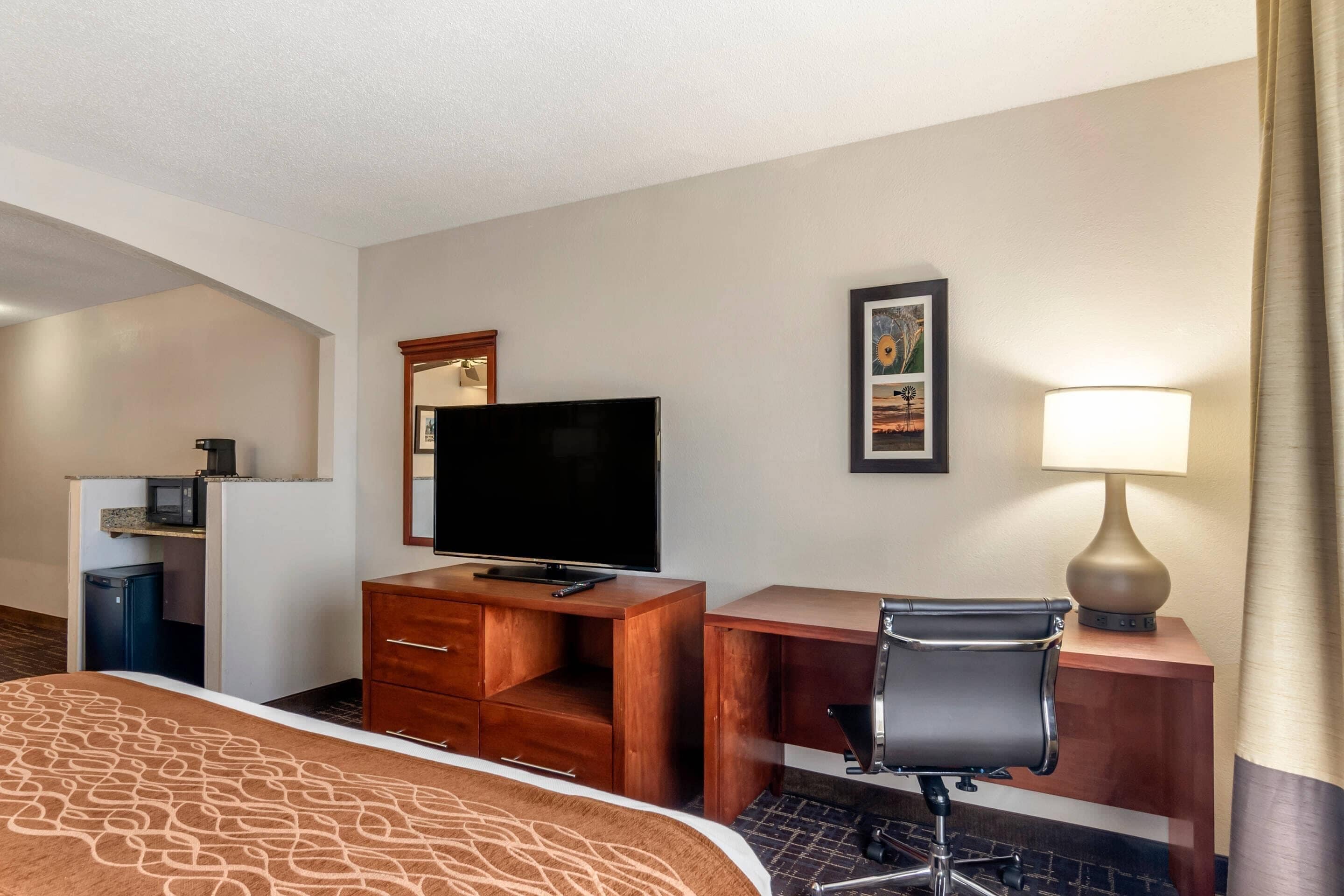 Ein Hotelzimmer mit einem Bett, einem Schreibtisch mit Stuhl, einem Fernseher, einer Schreibtischlampe und einer kleinen Küchenzeile.