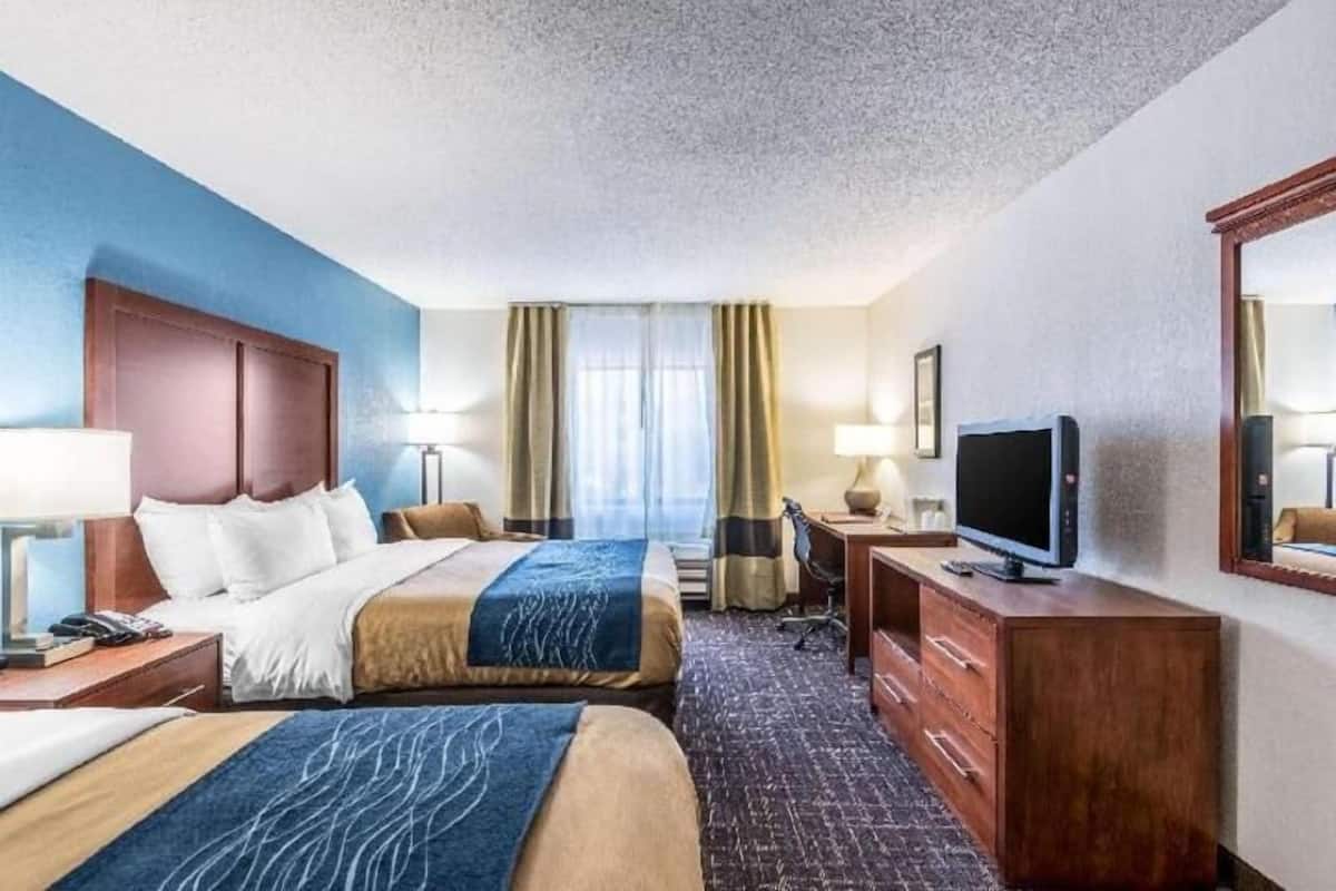A hotel room with two beds, a desk, a TV, and a mirror.