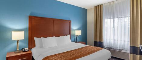 A hotel room with a large bed, two bedside tables with lamps, a window with curtains, and a wall painted blue.
