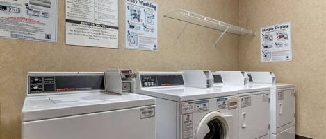A laundry area with multiple washers and dryers, safety instructions, and a clothes drying rack.