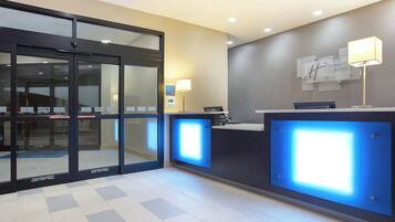 A hotel reception area with automatic sliding doors, a reception desk, and a wall-mounted sign.