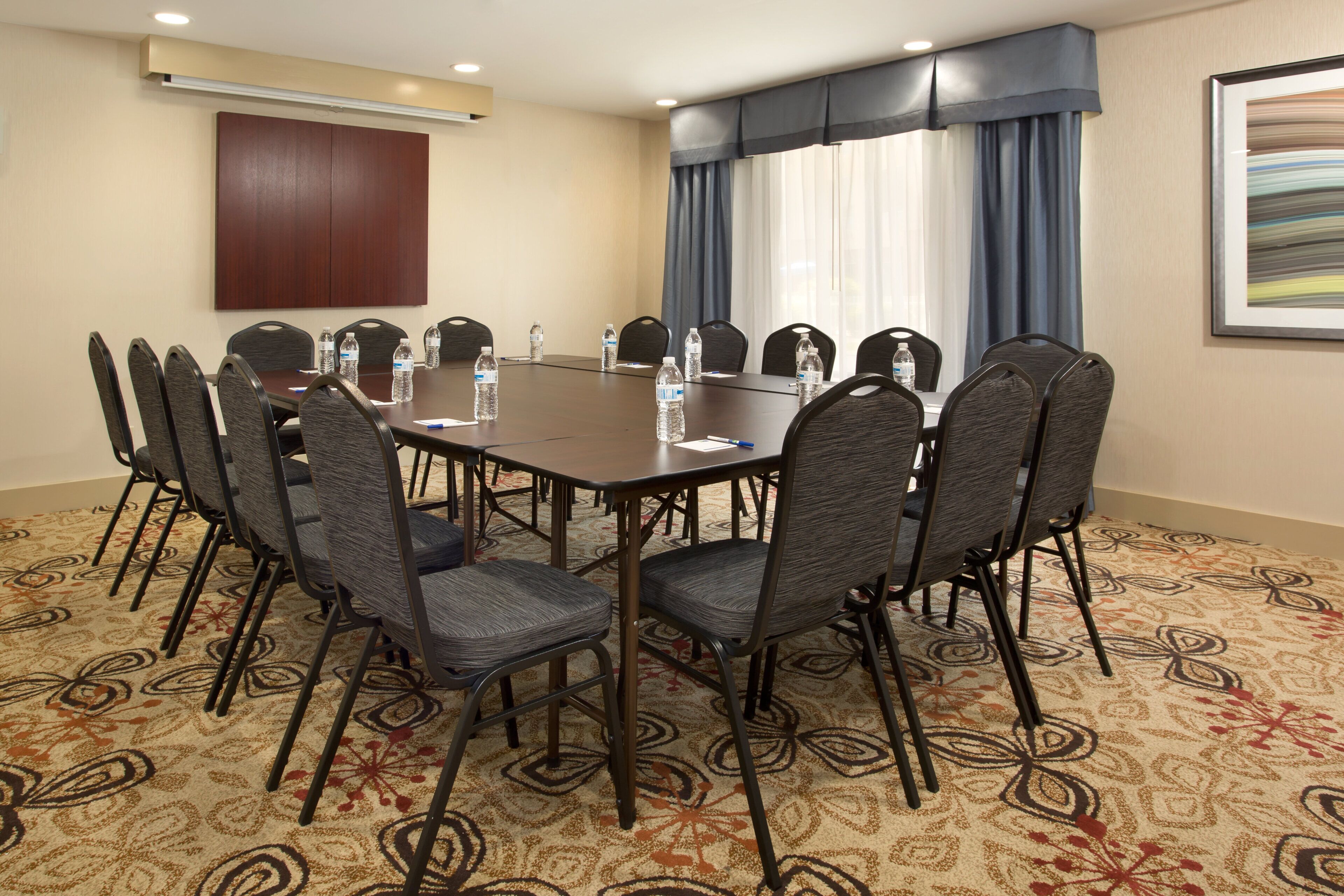 A conference room with a round table, chairs, water bottles, and a carpeted floor.